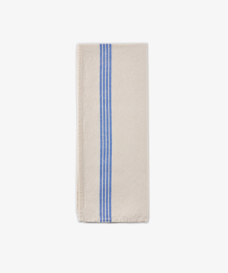 The Métis Tea Towel, crafted from a folded beige linen-cotton blend and adorned with three parallel blue stripes running vertically along one side, is displayed on a plain white background.