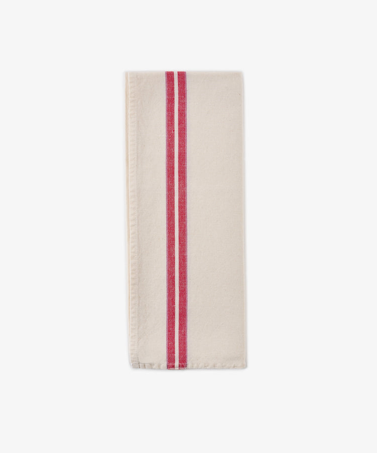 A folded Métis Tea Towel—cream-colored linen with two parallel red stripes running vertically near one edge, evocative of classic French kitchen linens—is displayed on a plain white background.