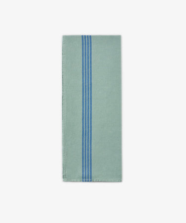 The Métis Tea Towel, a folded light green cloth featuring three vertical blue stripes near the center, is displayed on a plain white background and evokes the look of French kitchen linens and classic vintage striped tea towels.
