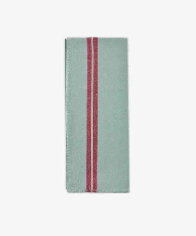 A folded light green Métis Tea Towel with two parallel red vintage stripes running vertically near the left edge, reminiscent of classic French kitchen linens, displayed on a plain white background.