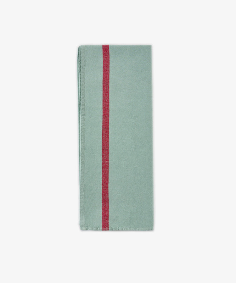 The Métis Tea Towel, in a folded light green hue and evoking vintage tea towel aesthetics, displays a single vertical red stripe near the left edge and is presented against a plain white background.