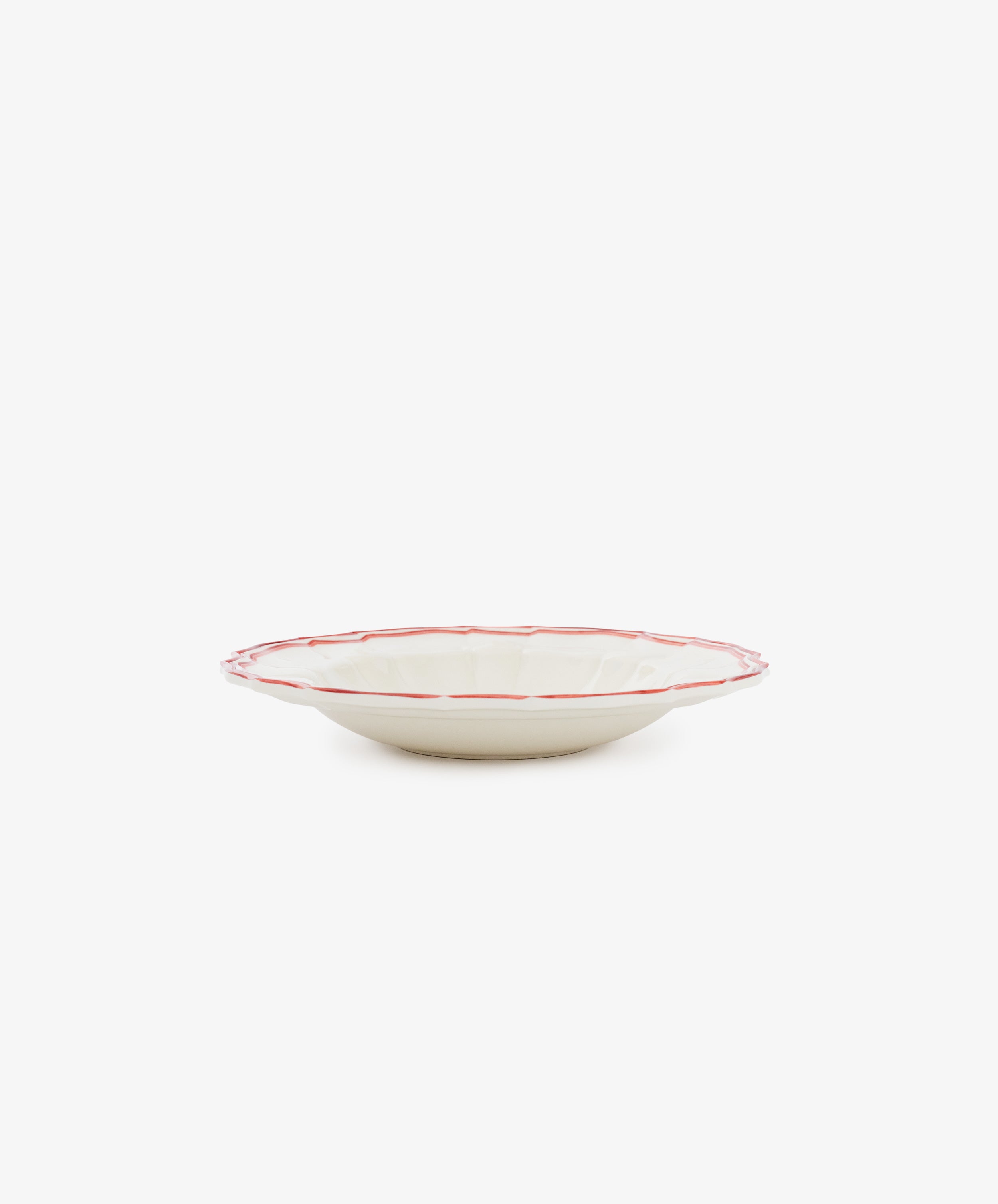 The Eva Melamine Bowl, Set of 4, features shallow, round cream-colored bowls with scalloped edges and red rims, inspired by Italian practicality. Photographed against a plain white background.