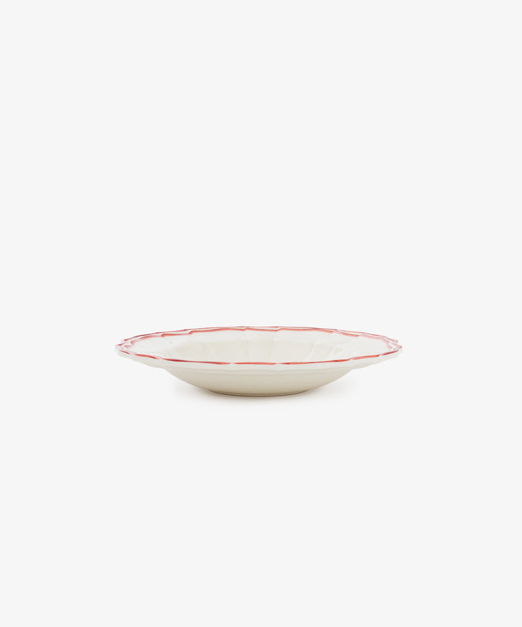 The Eva Melamine Bowl, Set of 4, features shallow, round cream-colored bowls with scalloped edges and red rims, inspired by Italian practicality. Photographed against a plain white background.