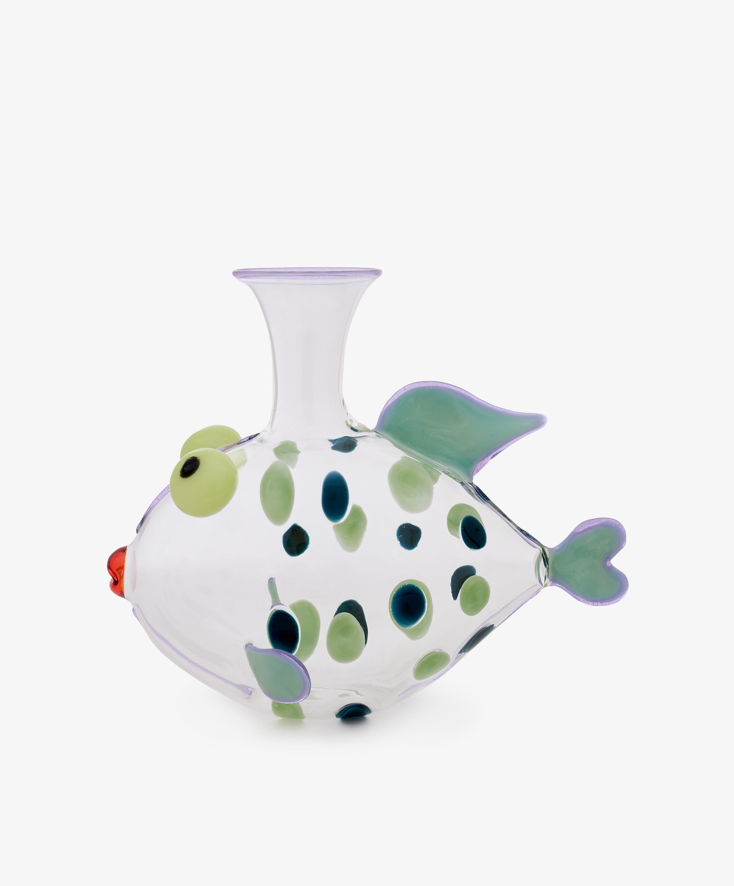 The Dotfish Decanter—crafted from clear glass and accented with green and blue spots, green fins, a red mouth, and raised round eyes—is inspired by Murano glass techniques. This whimsical fish-shaped vase is shown against a plain white background and evokes the playful design of Massimo Lunardon’s iconic Dotfish Decanter.