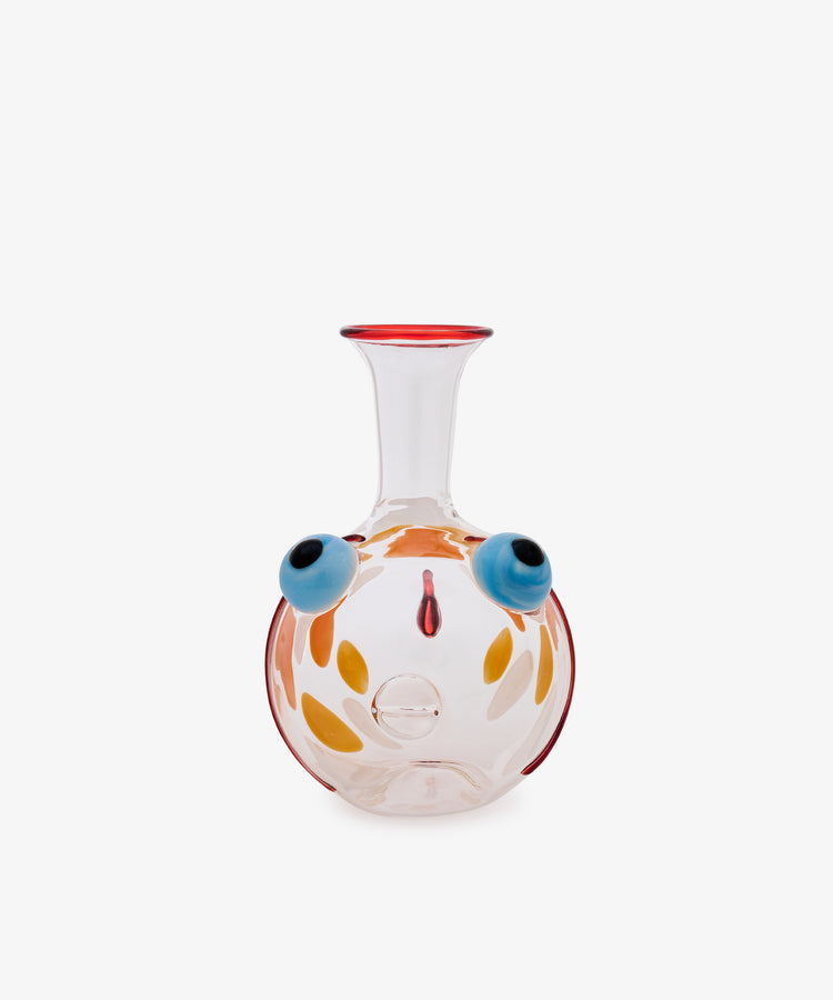 Fishpool Decanter crafted from clear Murano glass, featuring a wide round base and a narrow neck. The body is adorned with abstract, colorful designs reminiscent of facial features, including blue circular motifs and orange petal-like accents. Inspired by Massimo Lunardon’s whimsical artistry, this decanter channels the playful essence of his celebrated Fishpool collection.