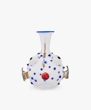 Pappagallo Decanter: Clear glass decanter shaped like a pufferfish, featuring cobalt blue spots, round eyes, gold fins, and a red mouth on a white background, reminiscent of Massimo Lunardon’s playful Murano glass designs.