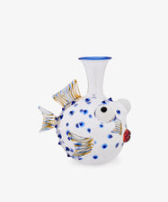 The Pappagallo Decanter, crafted from clear glass in the shape of a pufferfish and adorned with cobalt blue glass spots, gold-accented fins, and red lips reminiscent of whimsical Murano designs, is photographed against a plain white background.