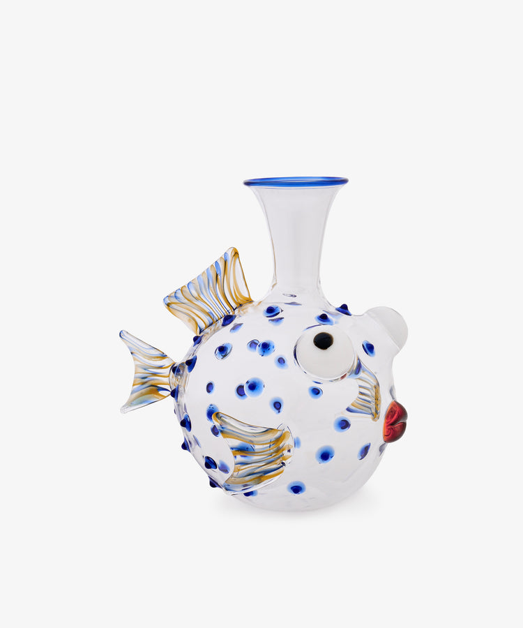 The Pappagallo Decanter, crafted from clear glass in the shape of a pufferfish and adorned with cobalt blue glass spots, gold-accented fins, and red lips reminiscent of whimsical Murano designs, is photographed against a plain white background.