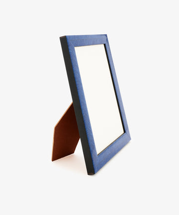 The Torino Frame, featuring a blank white display area bordered by a deep blue edge, is supported by a brown wooden stand and positioned at a slight rightward angle against a plain white background.
