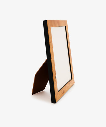 The Torino Frame, a wooden frame with a black edge and a stand, features subtle amber mustard tones and is displayed at an angle on a white background.