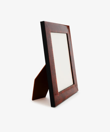 The Torino Frame, a wooden picture frame with a stand, is shown from an angled side view. It features rich geometric marquetry and has a blank space for displaying a photo, all set against a plain white background.