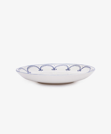 The Arco Serving Platter is a white ceramic plate with a low rim and a blue scalloped line pattern along the edge, inspired by traditional design, set against a plain white background.