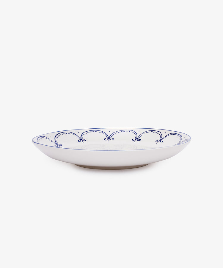 The Arco Serving Platter is a white ceramic plate with a low rim and a blue scalloped line pattern along the edge, inspired by traditional design, set against a plain white background.