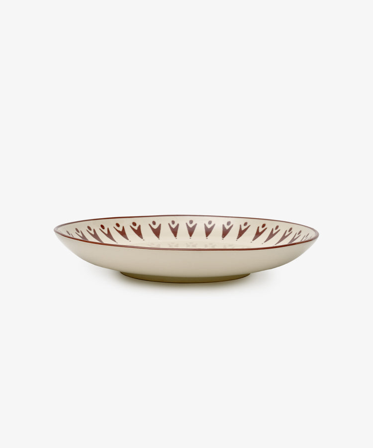 The Vito Serving Platter is a handmade, shallow round ceramic plate featuring a cream base and a brown rim with heart-shaped patterns.