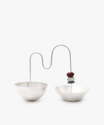 The Astrid Aperitivo Set features two geometric silver metal bowls joined by a curved rod with two stacked beads, showcasing Italian craftsmanship—an elegant addition to any setting.