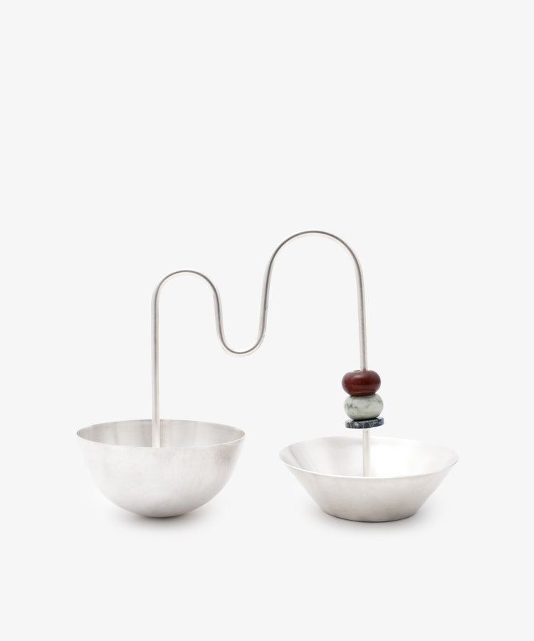 The Astrid Aperitivo Set features two geometric silver metal bowls joined by a curved rod with two stacked beads, showcasing Italian craftsmanship—an elegant addition to any setting.