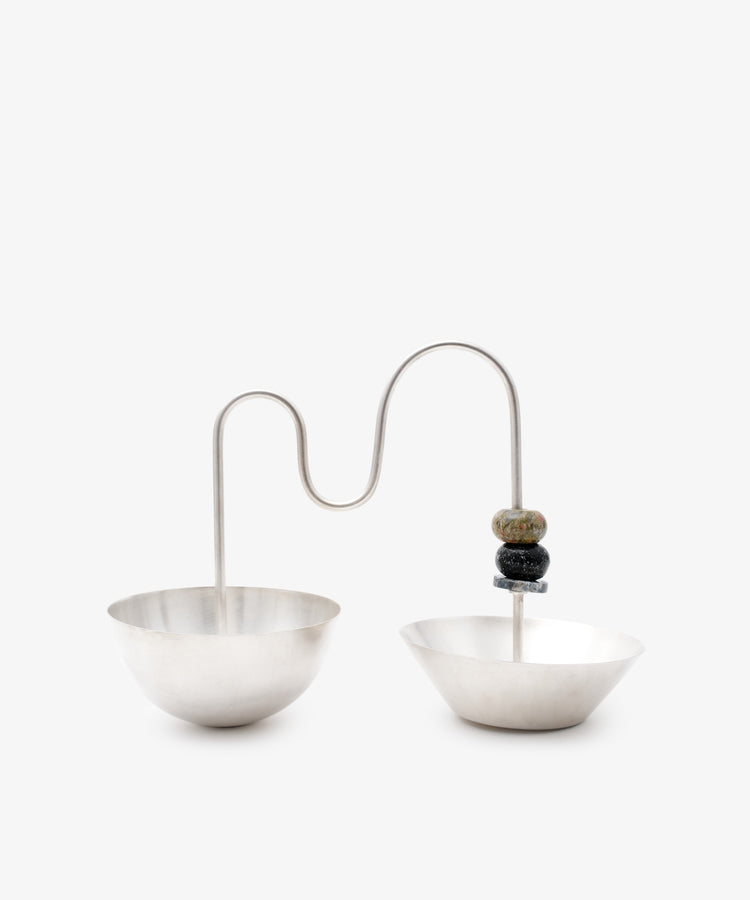 The Astrid Aperitivo Set features two geometric bowls linked by a curved metal rod with three stone-like beads on one side, all set against a white background—an elegant display of modern Italian design.