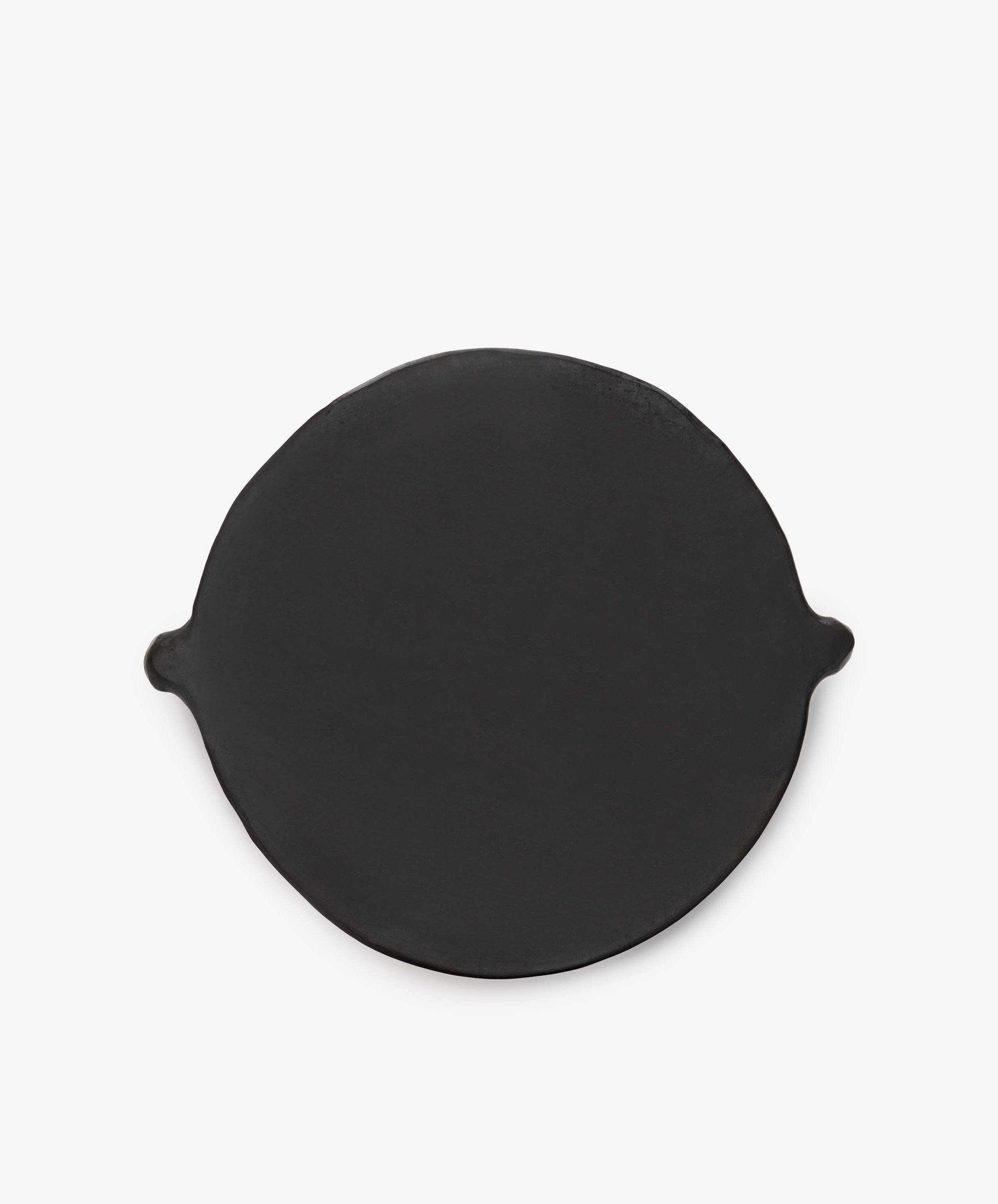 The Chamba Fruit Bowl is a round, flat, black cast iron piece with two small side handles, inspired by handmade Colombian pottery and shown on a plain white background.