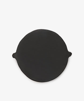 The Chamba Fruit Bowl is a round, flat, black cast iron piece with two small side handles, inspired by handmade Colombian pottery and shown on a plain white background.