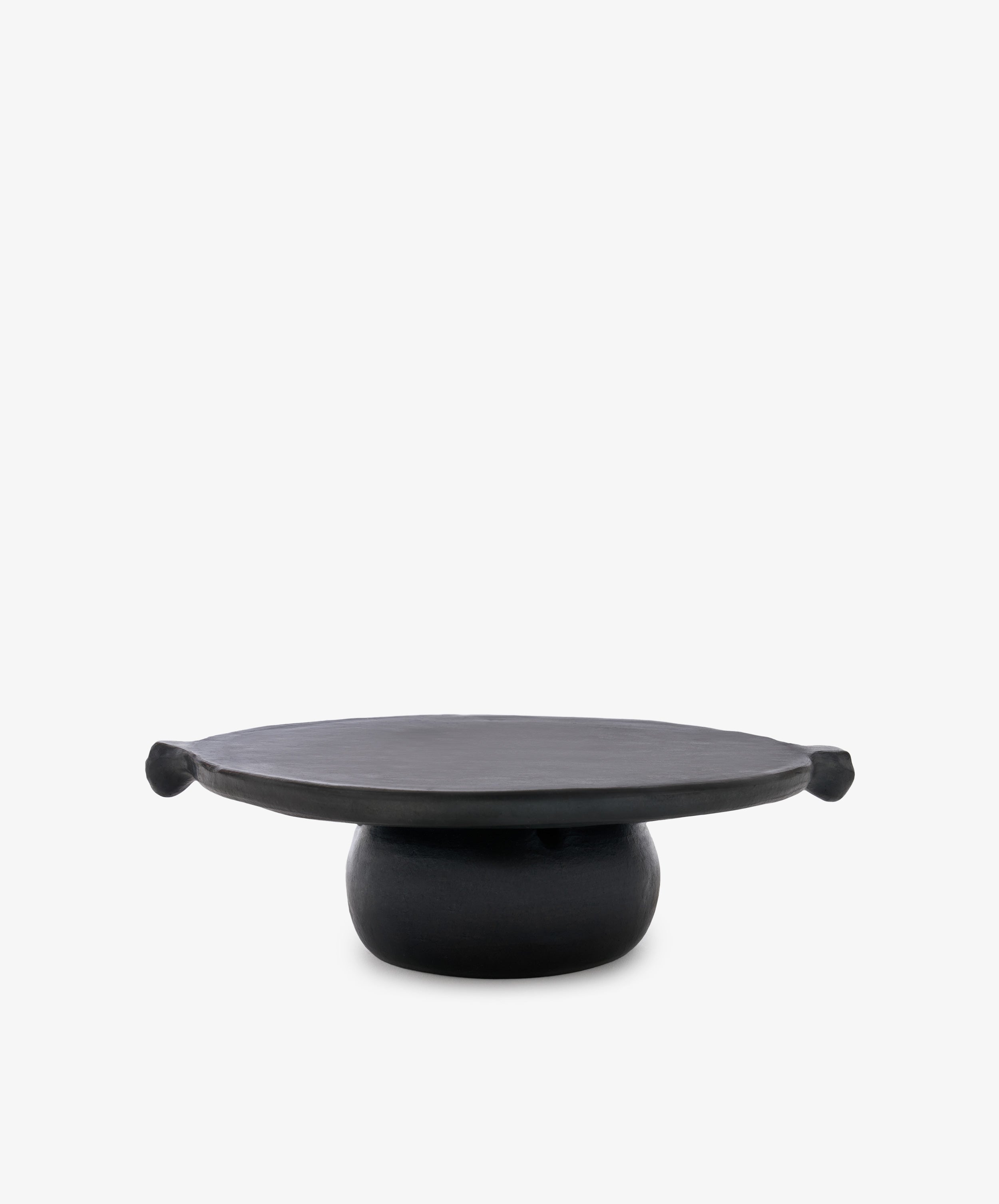 The Chamba Fruit Bowl is a black, round Colombian pottery pedestal plate with a wide flat top and two knob-like handles, beautifully handmade.