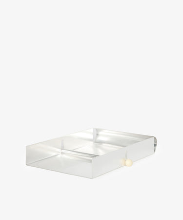 The Paper Holder is a clear acrylic rectangular desk tray with a small round white knob on one side, photographed on a plain white background, serving as a sleek paper holder and desk accessory.