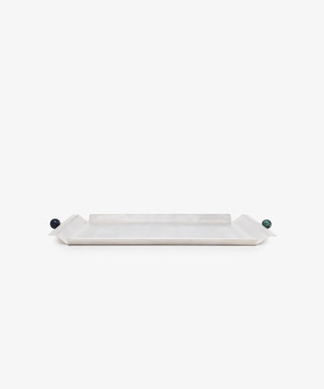 The Freya Serving Tray is a minimal tray with slightly raised angled ends and small round handles—one dark blue, one green—in a natural stone color, shown against a plain white background.