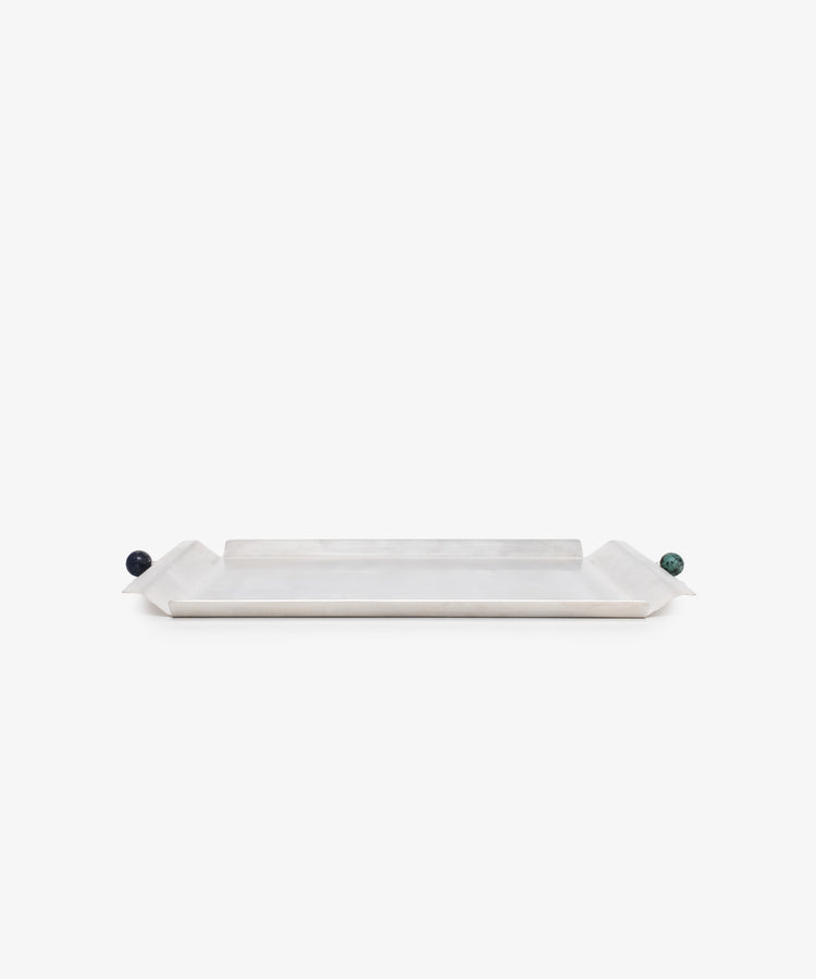 The Freya Serving Tray is a minimal tray with slightly raised angled ends and small round handles—one dark blue, one green—in a natural stone color, shown against a plain white background.