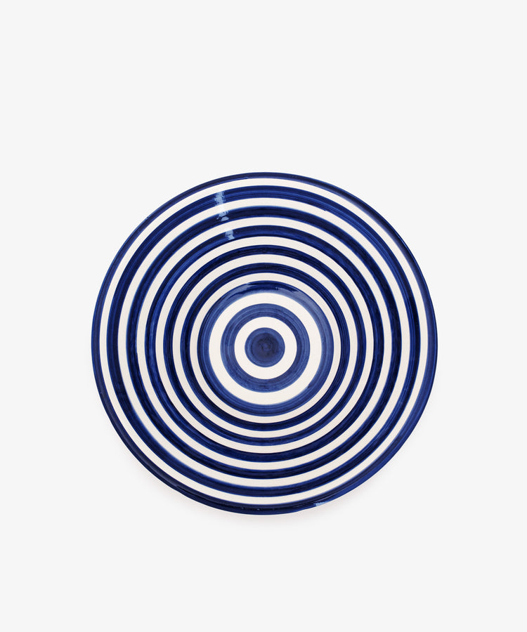 The Natalia Serving Bowl is a unique, round ceramic bowl featuring concentric navy blue and white rings on a white background, reminiscent of handcrafted striped designs.