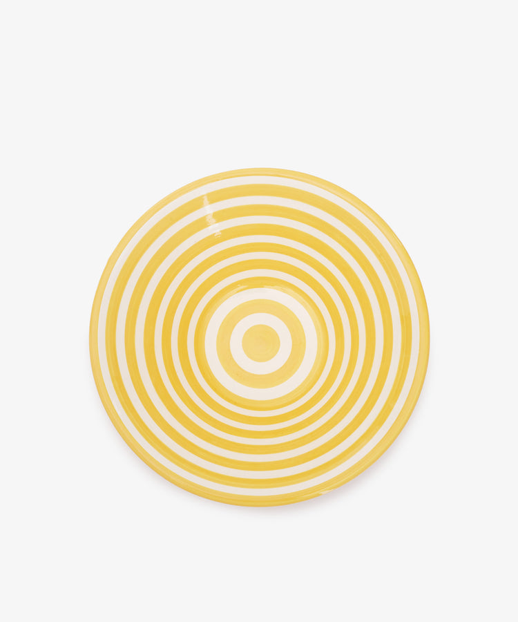 The Natalia Serving Bowl is a round, handmade piece with yellow and white concentric circles that stand out beautifully against a white background.