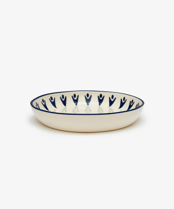 Vito Pasta Bowl. White stoneware shallow bowl with painted blue rim and design details, side view.