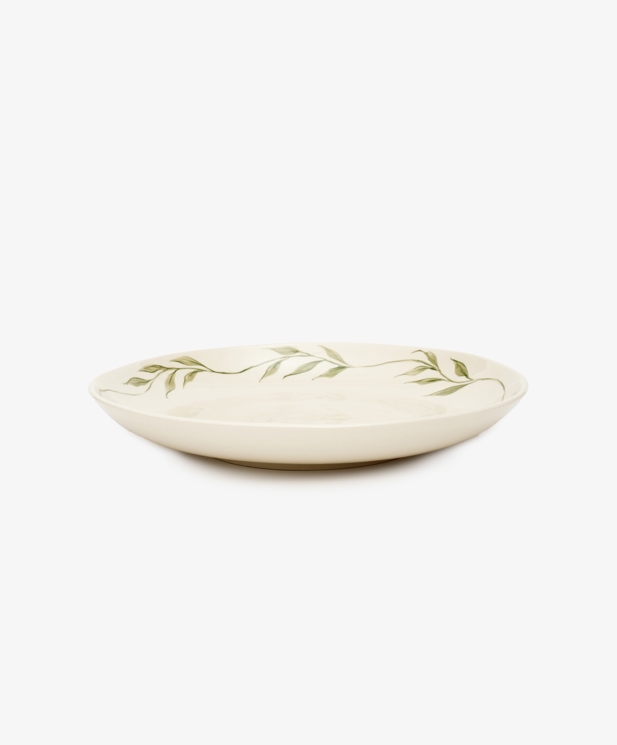 Penelope Serving Plate. Hand-painted stoneware plate in white with green vines border, side view.