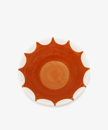 The Stella Serving Bowl is a round, handmade ceramic bowl featuring a white rim and a central orange-brown sunburst pattern, shown against a plain white background.