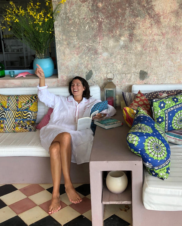 Woman sitting on a cushioned bench with colorful pillows, smiling and holding a book.