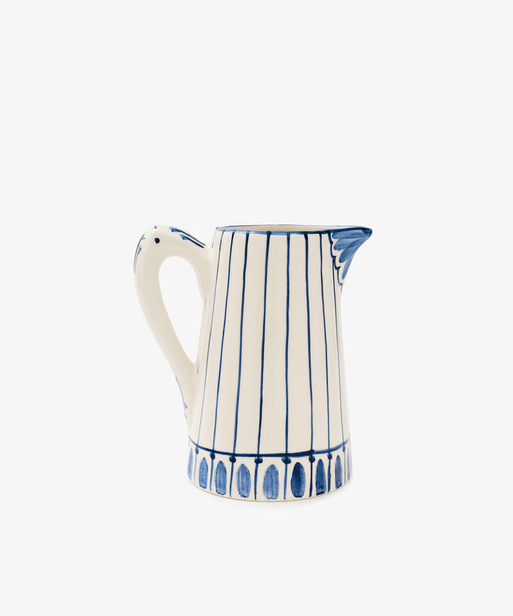 The Jorge Jug is a white ceramic Portuguese jug with blue vertical stripes in a traditional pattern, featuring a curved handle and a blue accent near the spout, set against a plain white background.