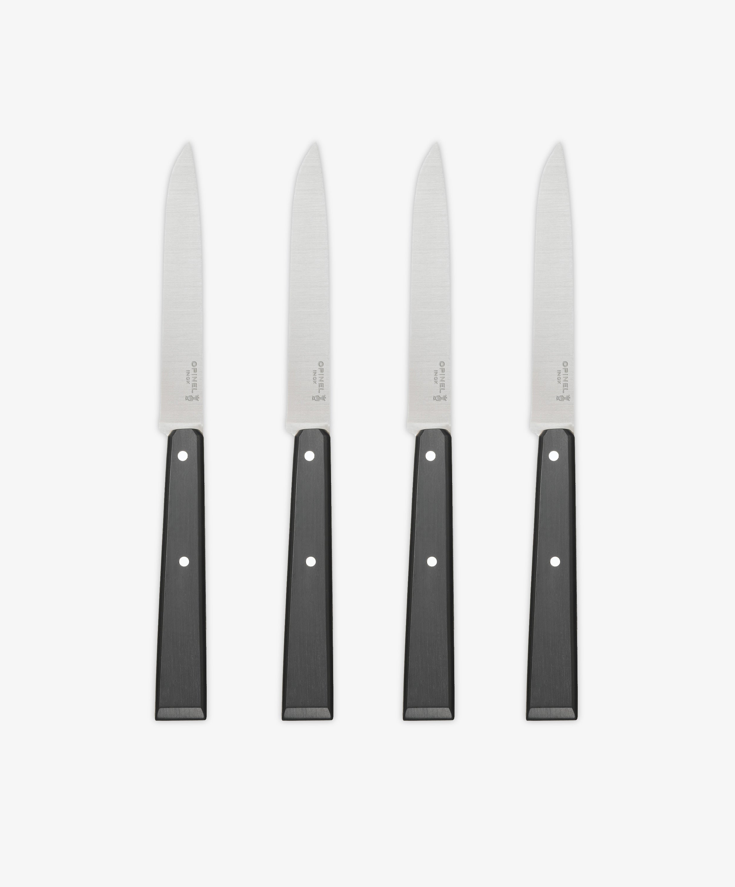 A set of four Micro-Serrated Steak Knives with stainless steel blades and black handles are arranged upright in a row on a white background.