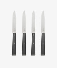 A set of four Micro-Serrated Steak Knives with stainless steel blades and black handles are arranged upright in a row on a white background.
