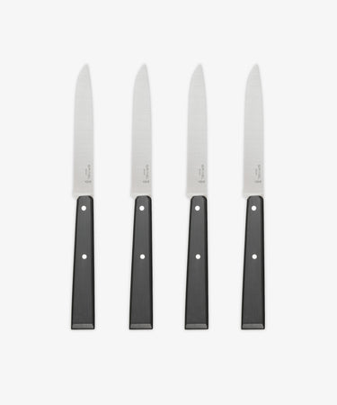 A set of four Micro-Serrated Steak Knives with stainless steel blades and black handles are arranged upright in a row on a white background.