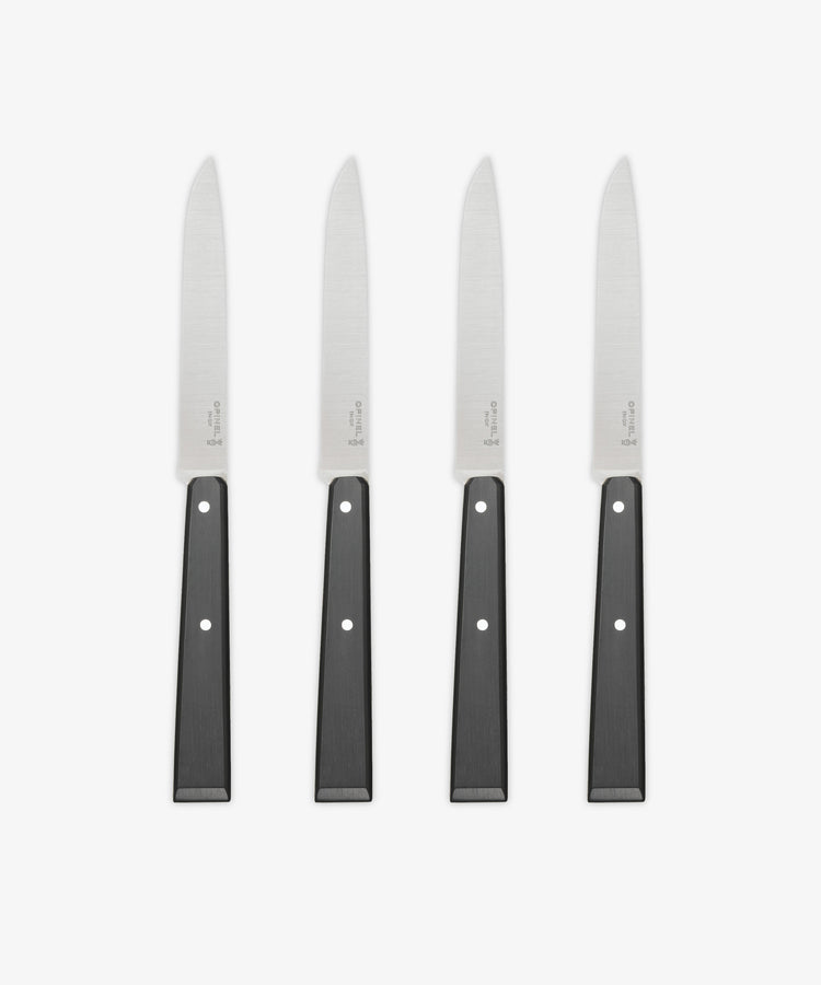 A set of four Micro-Serrated Steak Knives with stainless steel blades and black handles are arranged upright in a row on a white background.