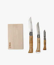 The Nomad Kit with Bottle Opener Knife includes a wooden cutting board, two wooden-handled kitchen knives, and a vegetable peeler—an ideal portable cutlery set for your travel kitchen kit.