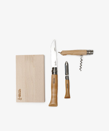 The Nomad Kit with Bottle Opener Knife features a wooden cutting board, knife, vegetable peeler, and corkscrew with wooden handles, all displayed on a white background as a compact travel kitchen set.