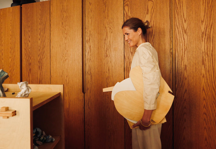 Smiling woman carrying wooden boards shaped like palettes in front of a wooden wall.