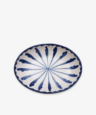 The Rayas Oval Serving Platter is a handmade ceramic piece featuring a blue and white radial feather-like pattern on the interior, highlighting its unique artistry.