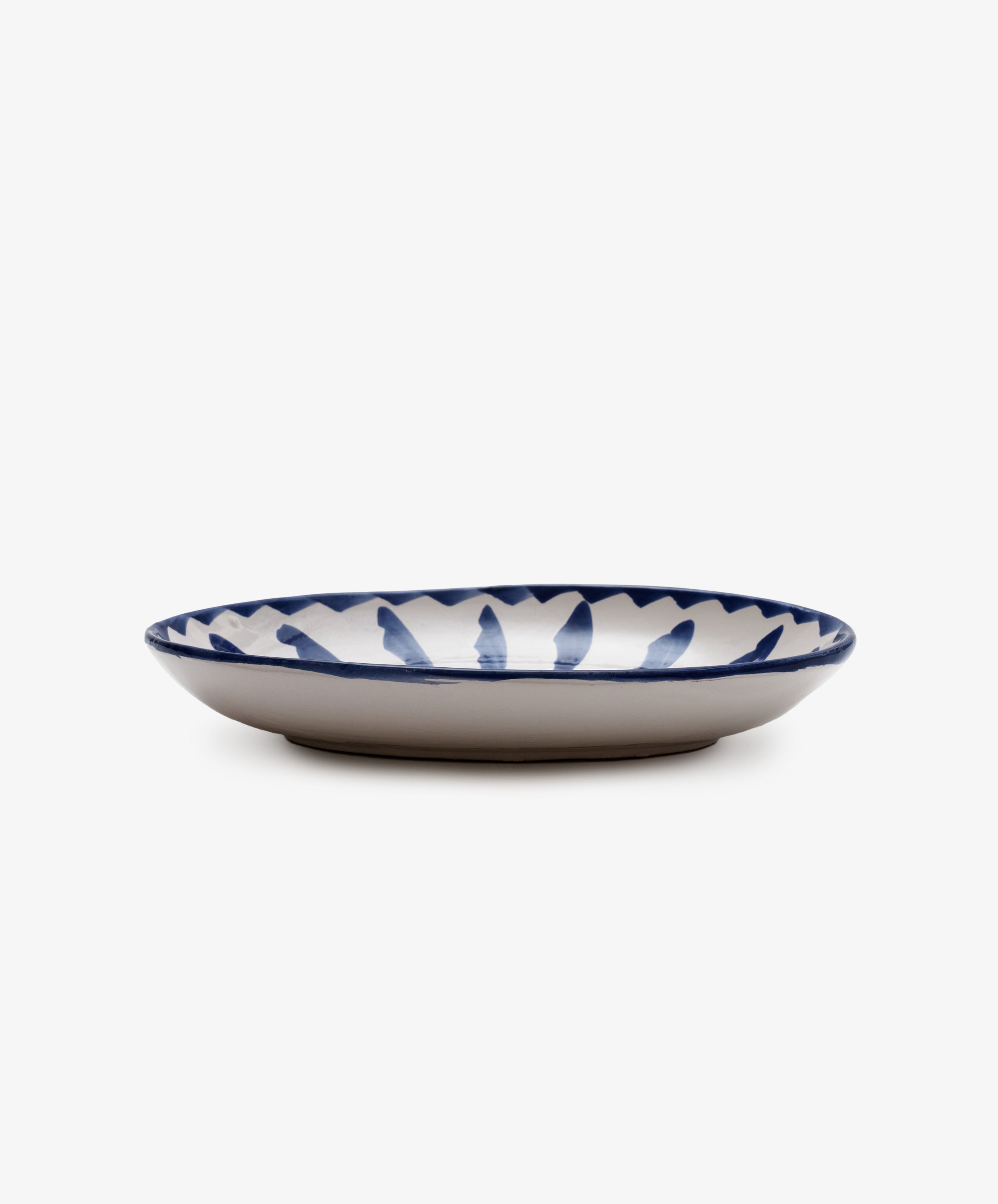 The Rayas Oval Serving Platter is a handmade ceramic piece with a white base and vibrant blue hand-painted leaf design around the rim, perfect for stylish serving.