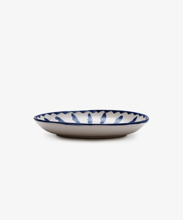 The Rayas Oval Serving Platter is a shallow handmade ceramic plate with a white base and a vibrant blue leaf-like rim pattern, shown against a plain white background.