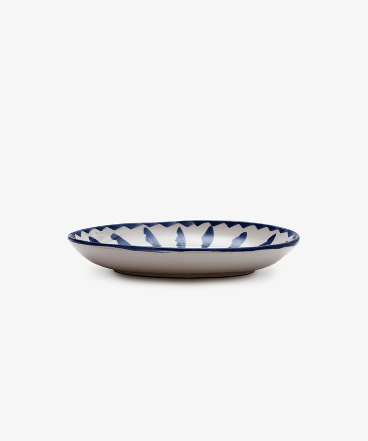 The Rayas Oval Serving Platter is a shallow handmade ceramic plate with a white base and a vibrant blue leaf-like rim pattern, shown against a plain white background.