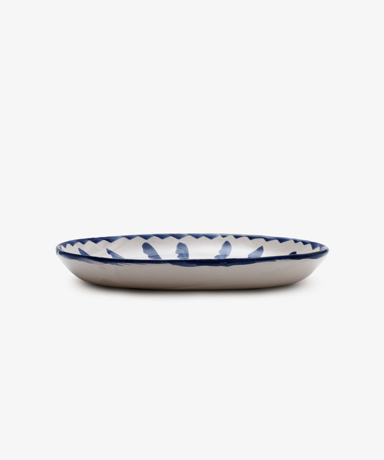 The Rayas Oval Serving Platter is a unique handmade ceramic plate featuring a white base and a vibrant blue hand-painted pattern around the rim, displayed against a white background.