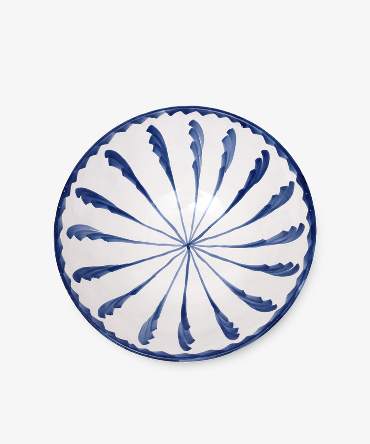 The Rayas Serving Bowl is a round ceramic piece, hand-painted with a blue leaf-like radial pattern on a white base, highlighting its unique handmade charm.