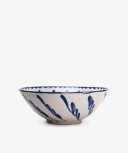 The Rayas Serving Bowl is a wide ceramic piece with a white base and blue abstract brushstroke patterns on the rim and sides, hand-painted and photographed against a plain white background.