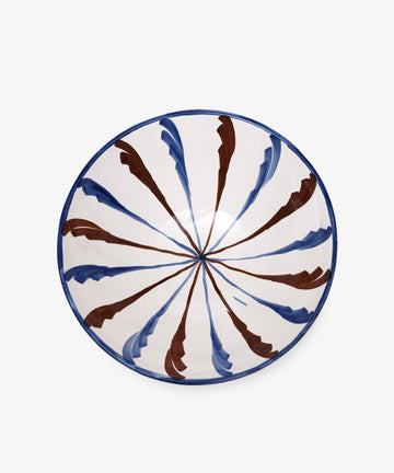 The Rayas Serving Bowl is a handmade round ceramic bowl with a white base and vibrant blue and brown brushstroke patterns radiating from the center, adding a splash of color to any setting.