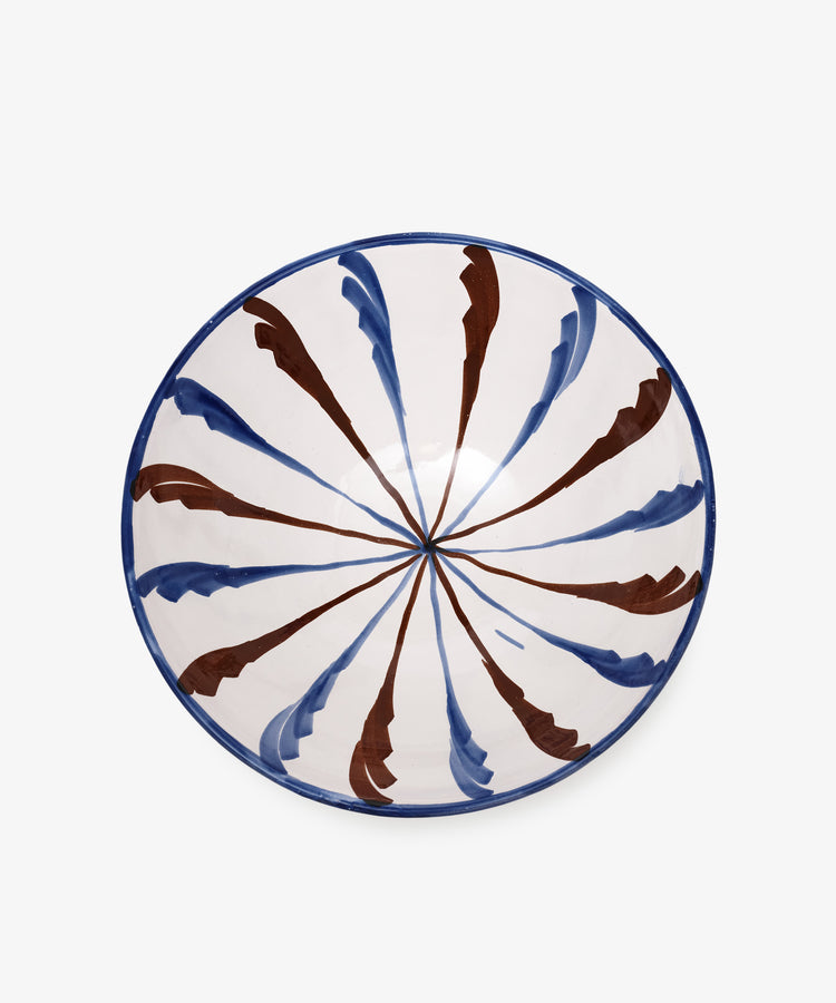 The Rayas Serving Bowl is a handmade round ceramic bowl with a white base and vibrant blue and brown brushstroke patterns radiating from the center, adding a splash of color to any setting.